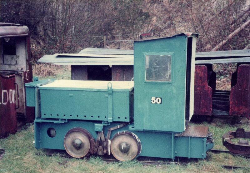 wr5031-53-brockham-070282.jpg - Wingrove & Rogers BEV 5031/1953 was the least viable of the three similar locos in the collection, although arguably the most interesting with its extended footplate and cab, and has therefore been used as a source of spares to keep the other two battery locos in service. Behind can be seen one of the Penrhyn quarrymen's coaches. The heap of rust on the left is the Fowler Resilient, "Peldon". 
 
The numbers on the sides of most of the Brockham exhibits were those allocated as a means of identification by the Trust and had no other significance, although some of the numbers did appear in various publications from time to time and have, rather confusingly, been perputuate by some.
